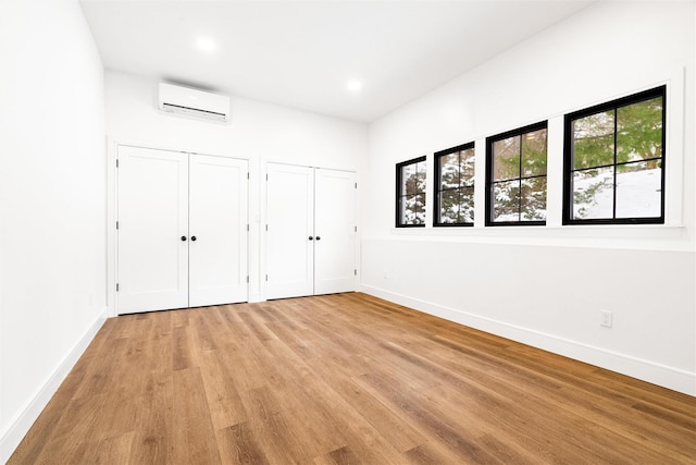 unfurnished bedroom featuring multiple closets, a wall unit AC, and light hardwood / wood-style floors