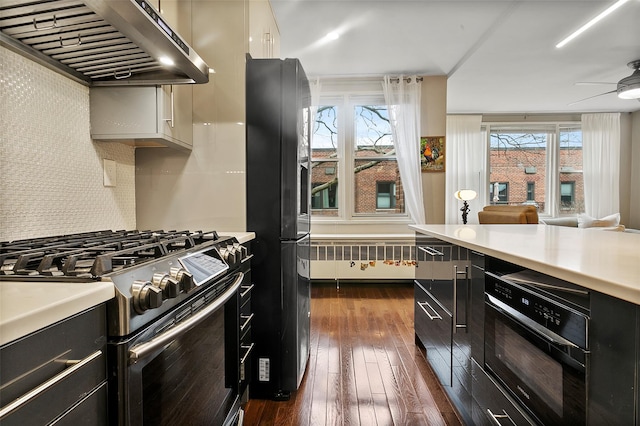 kitchen with radiator heating unit, wall oven, ventilation hood, black fridge, and gas range