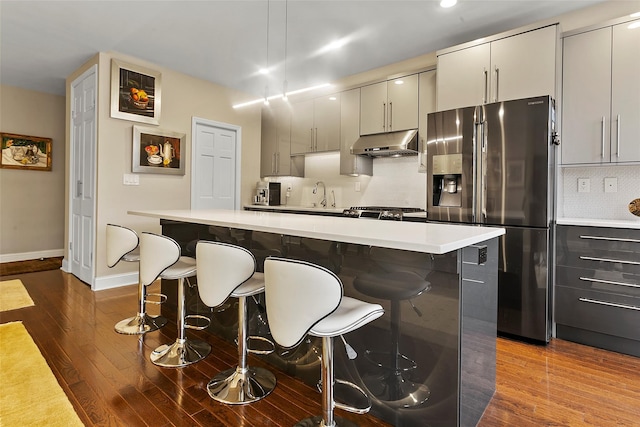 kitchen with wood-type flooring, a kitchen bar, decorative backsplash, stove, and stainless steel fridge with ice dispenser