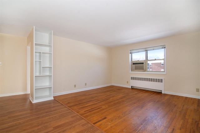 empty room with cooling unit, radiator heating unit, and wood-type flooring