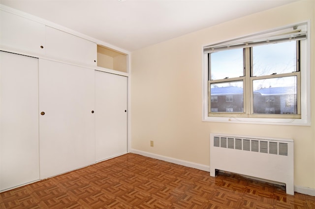 unfurnished bedroom with dark parquet flooring, radiator heating unit, and a closet