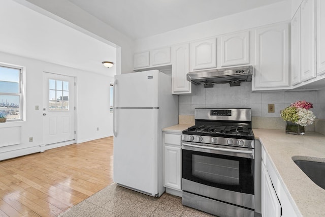 kitchen featuring stainless steel range with gas cooktop, white cabinets, backsplash, white refrigerator, and light hardwood / wood-style floors