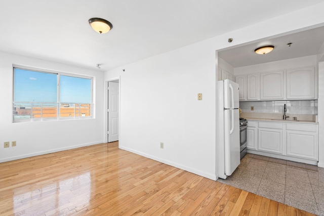 kitchen featuring stainless steel range with gas cooktop, white cabinetry, sink, decorative backsplash, and white refrigerator