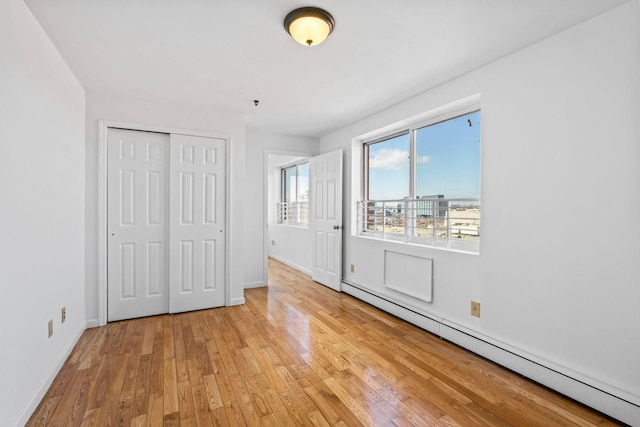 unfurnished bedroom featuring a baseboard radiator, a closet, and light wood-type flooring