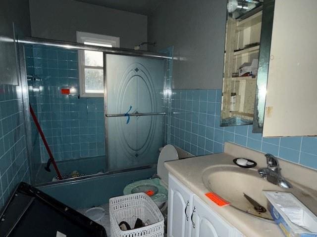 bathroom with bath / shower combo with glass door, tile walls, and vanity