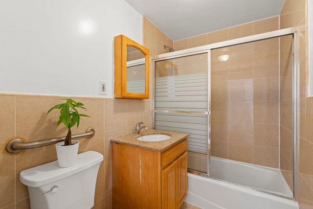 full bathroom featuring bath / shower combo with glass door, tile walls, vanity, and toilet