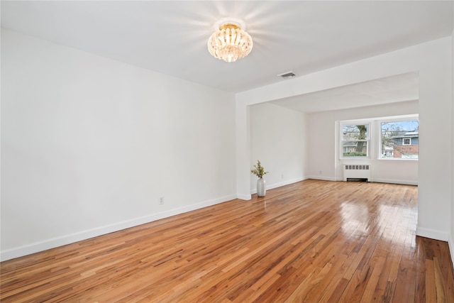 empty room with radiator heating unit, a notable chandelier, and light hardwood / wood-style floors