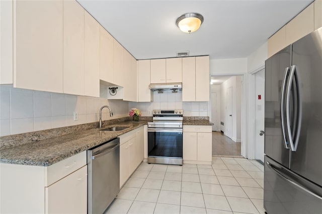 kitchen with sink, dark stone countertops, appliances with stainless steel finishes, decorative backsplash, and cream cabinetry