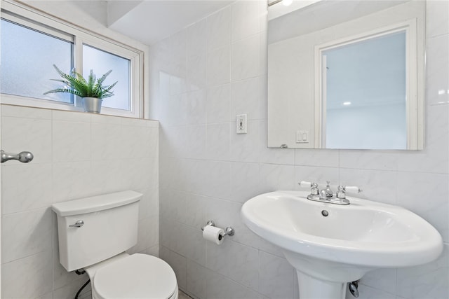 bathroom with toilet, sink, and tile walls