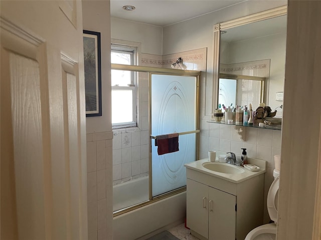 bathroom featuring toilet, backsplash, combined bath / shower with glass door, vanity, and tile walls