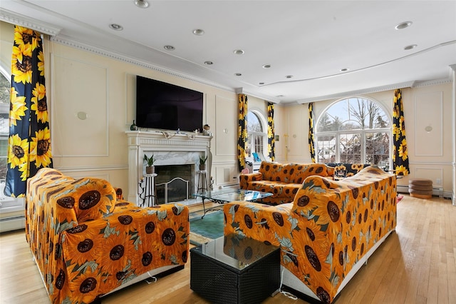 living room featuring light wood-type flooring, a high end fireplace, a baseboard heating unit, and ornamental molding