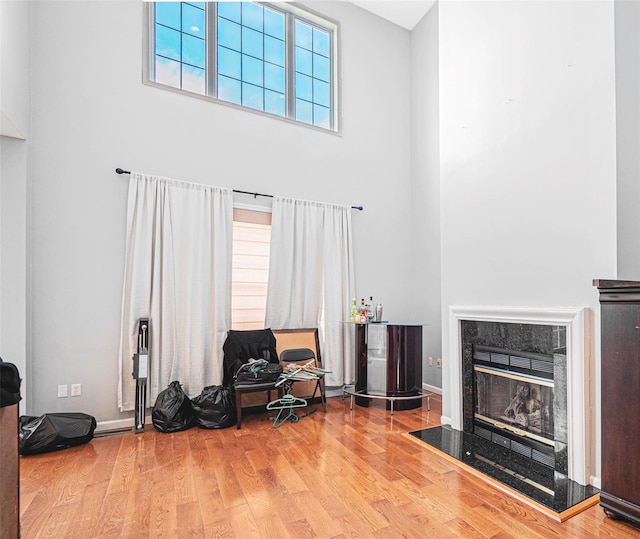 sitting room featuring a towering ceiling, a fireplace, and light wood-type flooring