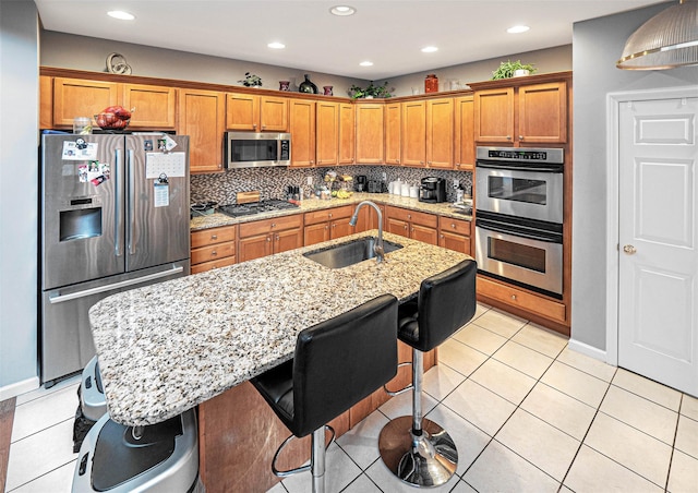 kitchen with sink, light tile patterned floors, a breakfast bar area, appliances with stainless steel finishes, and a kitchen island with sink