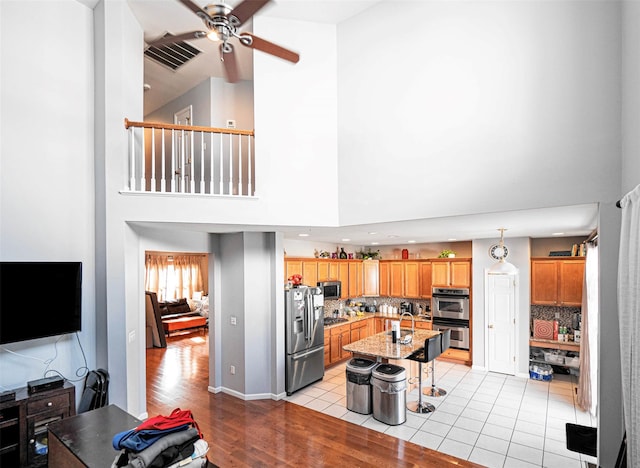 kitchen with backsplash, a kitchen breakfast bar, hanging light fixtures, stainless steel appliances, and a center island with sink