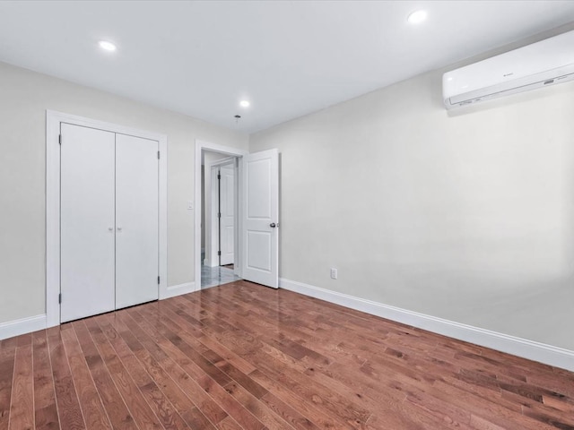 unfurnished bedroom featuring hardwood / wood-style flooring, an AC wall unit, and a closet