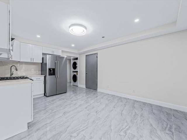 kitchen with high end fridge, backsplash, white cabinets, and stacked washing maching and dryer