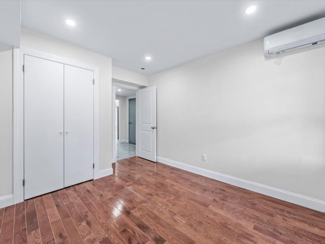 unfurnished bedroom featuring wood-type flooring, a wall unit AC, and a closet