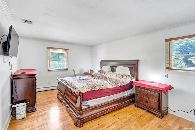 bedroom with multiple windows, a baseboard heating unit, and light wood-type flooring