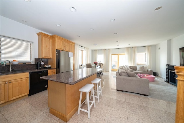 kitchen featuring stainless steel refrigerator, dishwasher, sink, dark stone countertops, and a center island