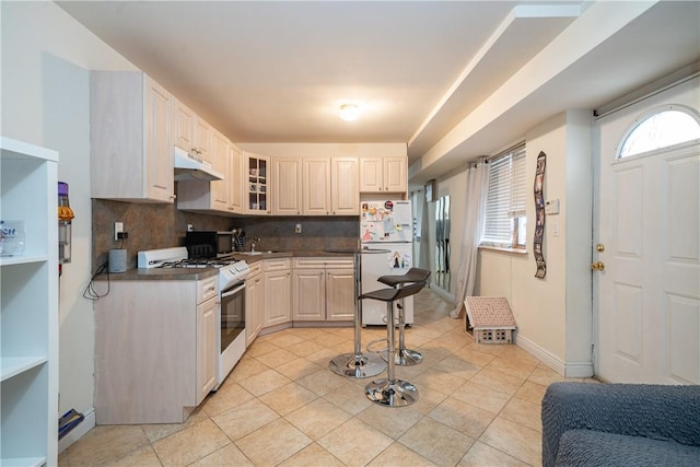 kitchen with light tile patterned flooring, white gas range, sink, and backsplash