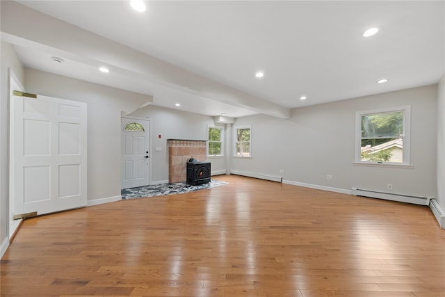 unfurnished living room with baseboard heating, a wood stove, and light wood-type flooring