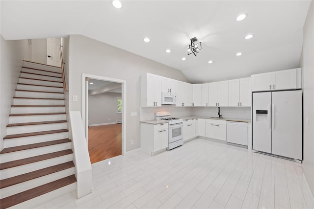 kitchen with sink, white appliances, light stone counters, white cabinets, and vaulted ceiling