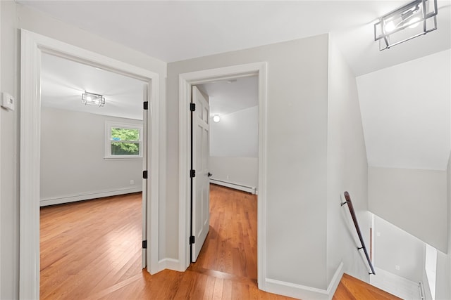 hall featuring lofted ceiling, light hardwood / wood-style floors, and a baseboard heating unit