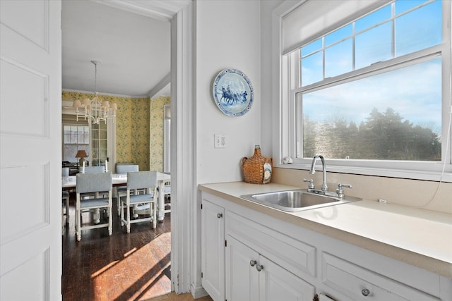 kitchen featuring sink, white cabinetry, wood-type flooring, a notable chandelier, and pendant lighting