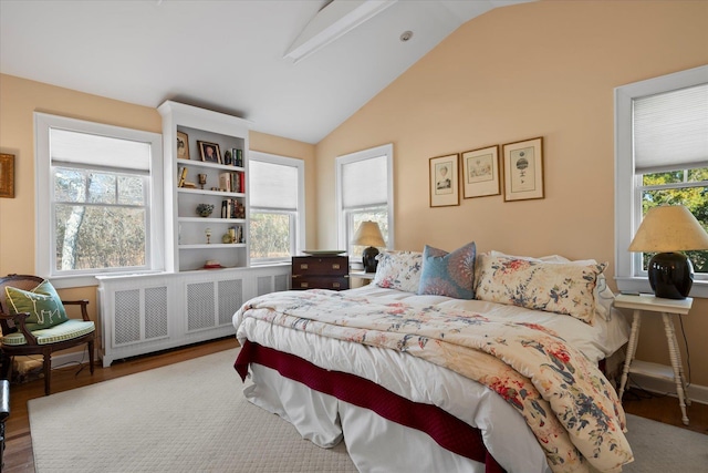 bedroom with multiple windows, vaulted ceiling, radiator, and hardwood / wood-style floors