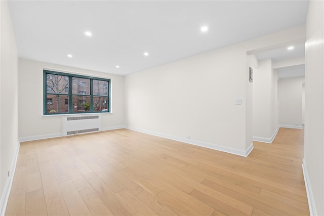 unfurnished living room featuring radiator heating unit and light hardwood / wood-style floors