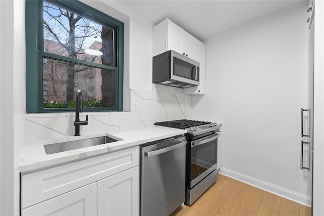 kitchen featuring sink, light wood-type flooring, stainless steel appliances, light stone countertops, and white cabinets