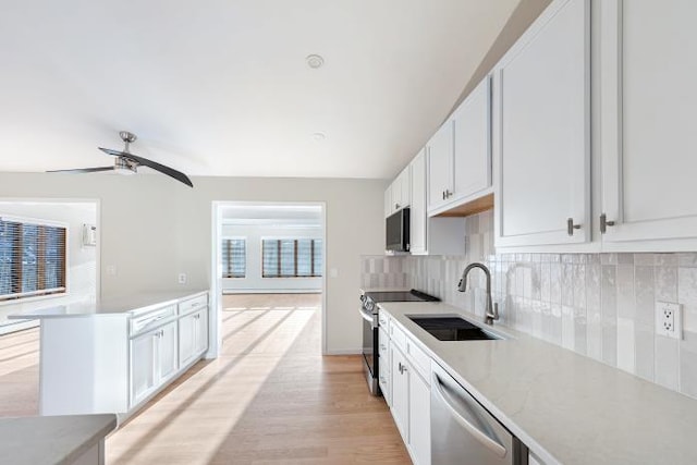 kitchen with appliances with stainless steel finishes, tasteful backsplash, white cabinetry, sink, and light wood-type flooring