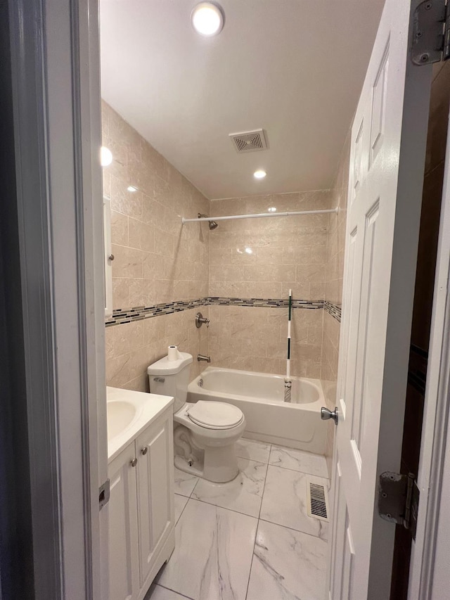 full bathroom featuring vanity, toilet, tiled shower / bath combo, and tile walls