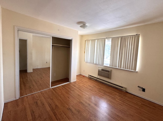 unfurnished bedroom featuring a baseboard heating unit, hardwood / wood-style flooring, a closet, and an AC wall unit