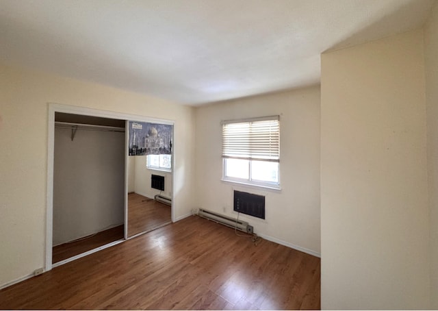 unfurnished bedroom with baseboard heating, a closet, and hardwood / wood-style flooring