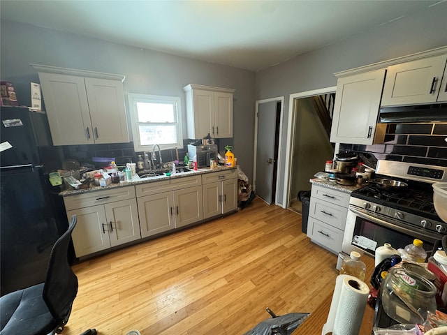 kitchen featuring sink, stainless steel gas stove, black refrigerator, light stone countertops, and light wood-type flooring