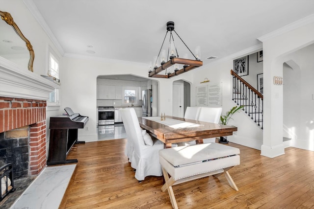 dining space featuring crown molding, a brick fireplace, and light hardwood / wood-style floors