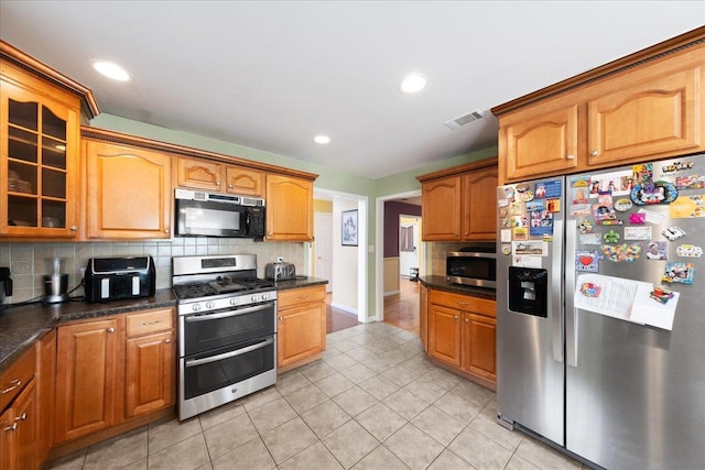 kitchen with dark stone countertops, appliances with stainless steel finishes, light tile patterned flooring, and backsplash