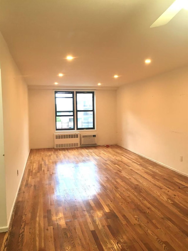 spare room featuring hardwood / wood-style flooring, radiator, and a wall unit AC