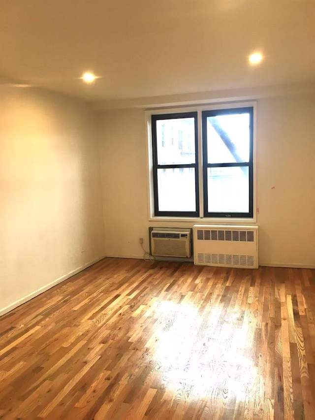 unfurnished room with wood-type flooring, an AC wall unit, and radiator