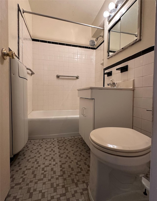 full bathroom with vanity, tiled shower / bath combo, toilet, and tile walls