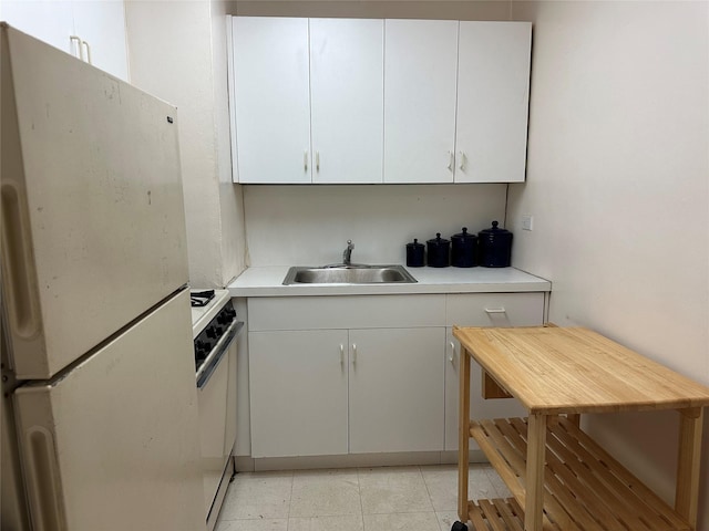 kitchen featuring white refrigerator, white cabinets, sink, and stove