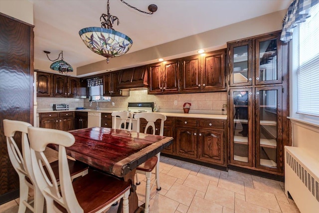 kitchen featuring pendant lighting, dishwasher, radiator heating unit, dark brown cabinetry, and decorative backsplash