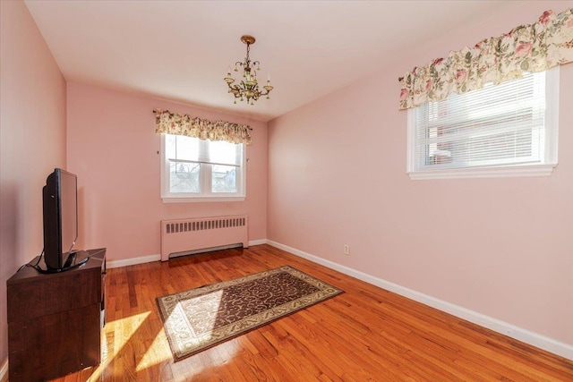 unfurnished room with hardwood / wood-style flooring, radiator heating unit, and a chandelier