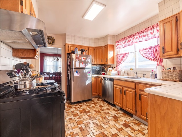 kitchen with sink, stainless steel appliances, tasteful backsplash, tile counters, and exhaust hood