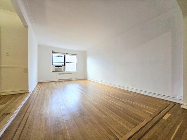 empty room featuring cooling unit, hardwood / wood-style floors, and radiator heating unit