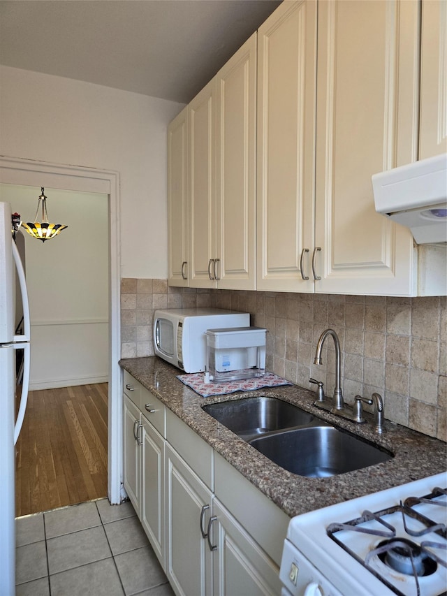 kitchen with sink, backsplash, dark stone counters, light tile patterned floors, and white appliances