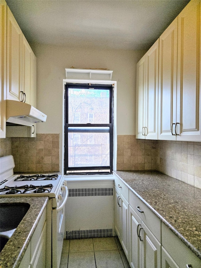 kitchen with radiator, backsplash, white gas range oven, and light tile patterned flooring