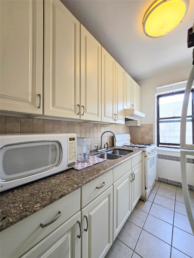 kitchen featuring radiator heating unit, sink, decorative backsplash, dark stone counters, and white appliances