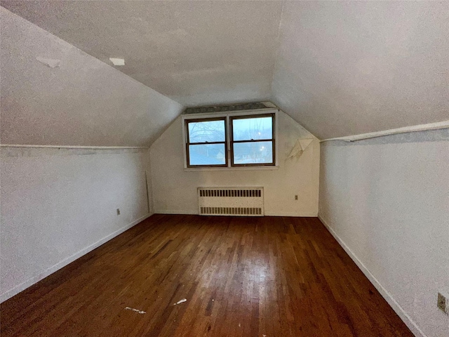 additional living space with vaulted ceiling, radiator, a textured ceiling, and dark hardwood / wood-style flooring